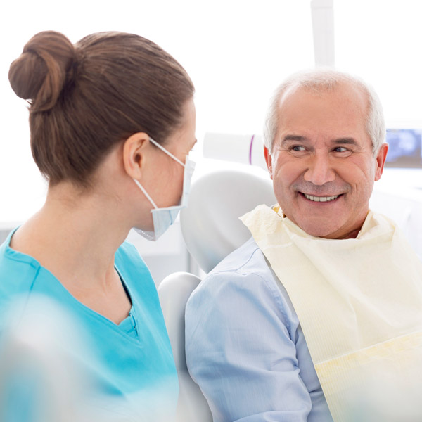 mature man sitting in dentist chair smiling at dentist