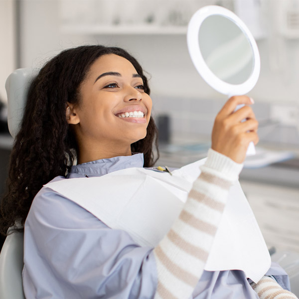 woman smiling in mirror while sitting in dental chair